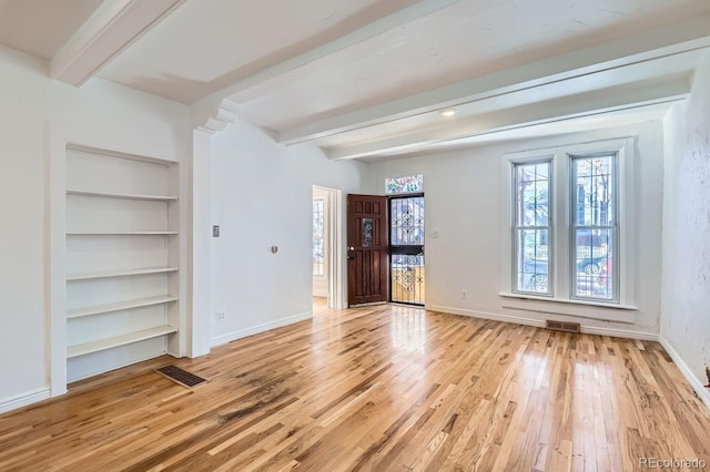 unfurnished room featuring beamed ceiling, built in shelves, and light hardwood / wood-style floors