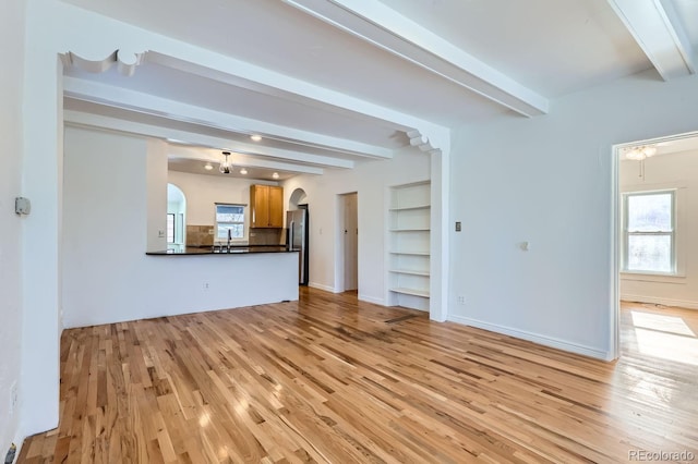 unfurnished living room featuring beam ceiling, built in shelves, sink, and light hardwood / wood-style flooring