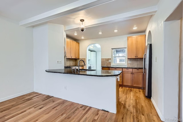 kitchen with kitchen peninsula, sink, stainless steel refrigerator, and tasteful backsplash