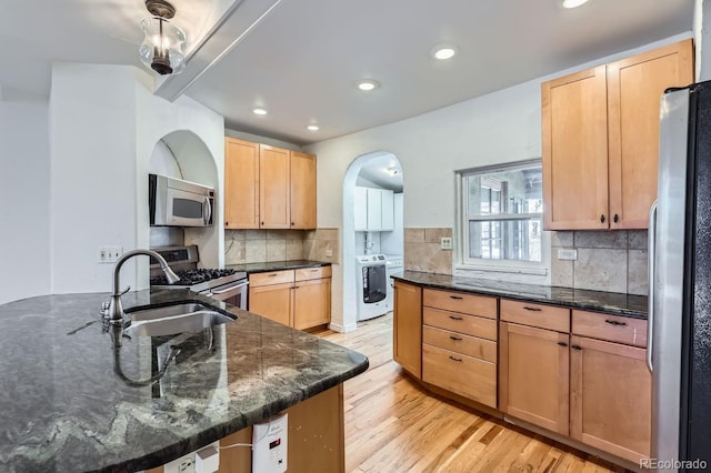 kitchen featuring sink, light hardwood / wood-style flooring, backsplash, dark stone countertops, and appliances with stainless steel finishes