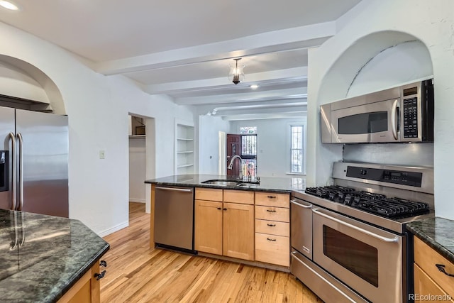 kitchen with beamed ceiling, appliances with stainless steel finishes, dark stone countertops, and sink