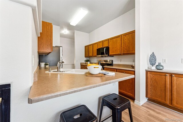 kitchen with sink, kitchen peninsula, a kitchen bar, appliances with stainless steel finishes, and light wood-type flooring