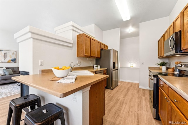 kitchen with kitchen peninsula, stainless steel appliances, sink, light hardwood / wood-style flooring, and a breakfast bar area