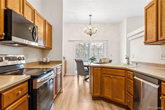 kitchen featuring appliances with stainless steel finishes, sink, decorative light fixtures, a chandelier, and light hardwood / wood-style floors