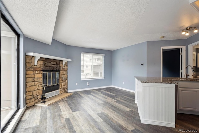 5250 S Huron Way Unit 1-204, Littleton, CO 80120 - unfurnished living room featuring a textured ceiling, a sink, dark wood-type flooring, baseboards, and a stone fireplace