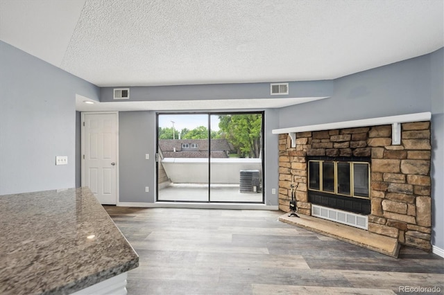 5250 S Huron Way Unit 1-204, Littleton, CO 80120 - unfurnished living room with wood finished floors, a stone fireplace, a textured ceiling, and baseboards