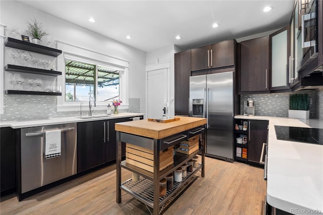 kitchen with dark brown cabinetry, sink, stainless steel appliances, light hardwood / wood-style floors, and backsplash