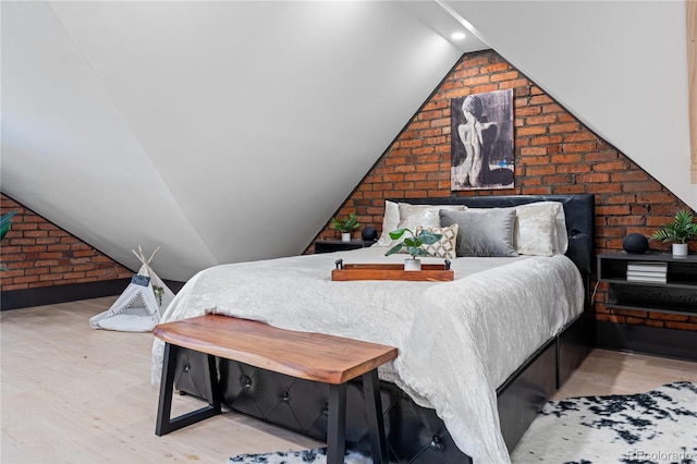 bedroom featuring vaulted ceiling, brick wall, and light hardwood / wood-style flooring