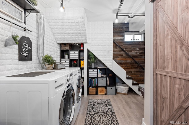 washroom with rail lighting, light hardwood / wood-style flooring, brick wall, a barn door, and washer and clothes dryer