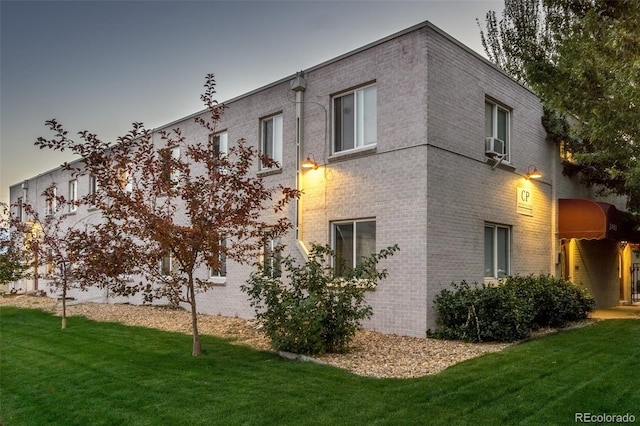 view of side of home with cooling unit, brick siding, and a lawn