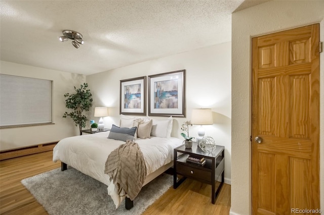 bedroom with baseboard heating, a textured ceiling, and wood finished floors