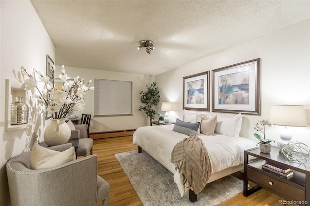 bedroom featuring light wood-type flooring, baseboard heating, and a textured ceiling