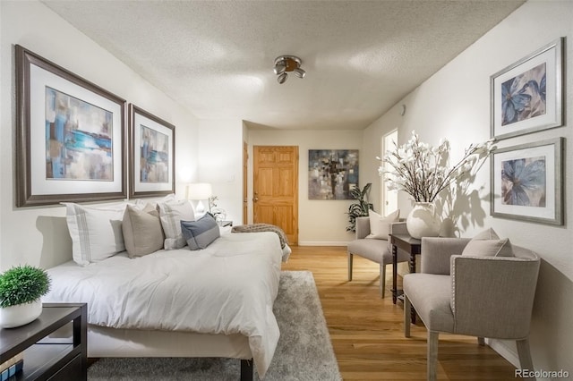 bedroom with baseboards, light wood finished floors, and a textured ceiling