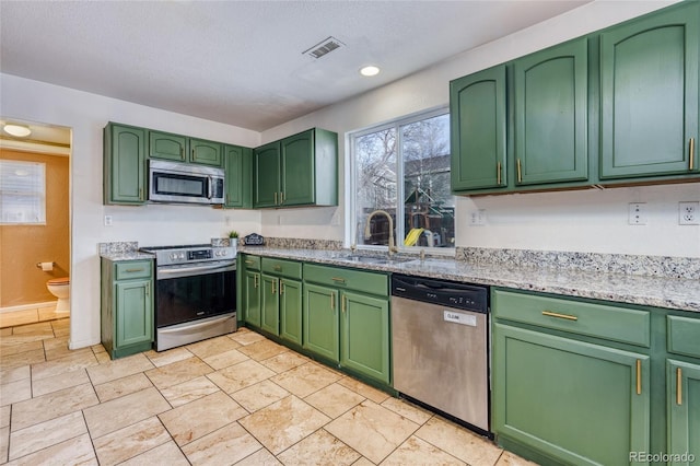 kitchen with sink, stainless steel appliances, green cabinetry, and light stone countertops