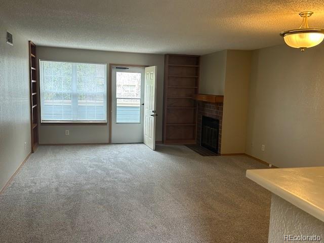 unfurnished living room featuring carpet floors, visible vents, a textured ceiling, and a tile fireplace