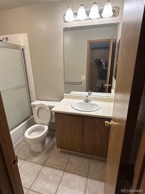 full bathroom featuring vanity, a textured wall, toilet, tile patterned floors, and combined bath / shower with glass door