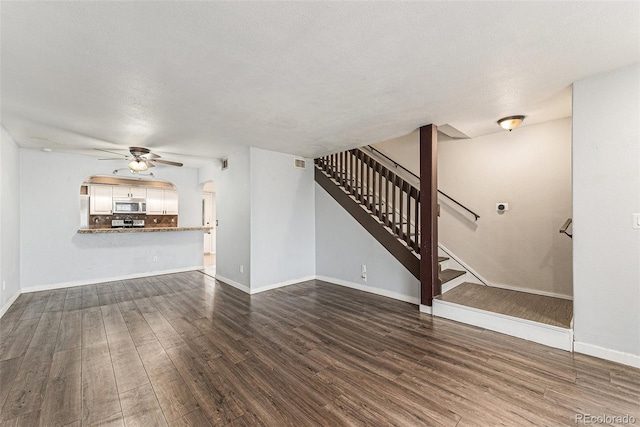 3550 S Harlan St Unit 105, Denver, CO 80235 - unfurnished living room with arched walkways, ceiling fan, dark wood-style floors, and stairs
