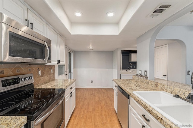 3550 S Harlan St Unit 105, Denver, CO 80235 - kitchen with stainless steel appliances, washer and clothes dryer, white cabinetry, light wood-style floors, and a wainscoted wall