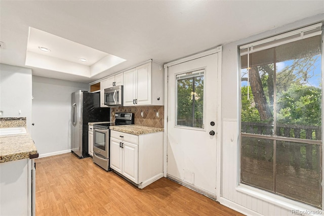 3550 S Harlan St Unit 105, Denver, CO 80235 - kitchen with appliances with stainless steel finishes, a tray ceiling, light wood-style floors, white cabinets, and light countertops