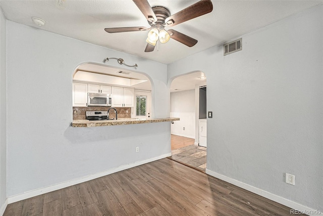 3550 S Harlan St Unit 105, Denver, CO 80235 - kitchen with stainless steel appliances, arched walkways, wood finished floors, a ceiling fan, and white cabinets