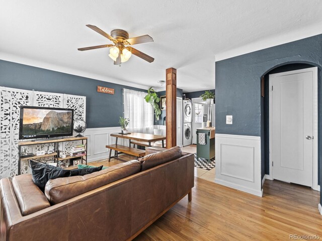 1221 Ulster St, Denver, CO 80220 - living area featuring estacked washer and dryer, a wainscoted wall, ceiling fan, a decorative wall, and wood finished floors