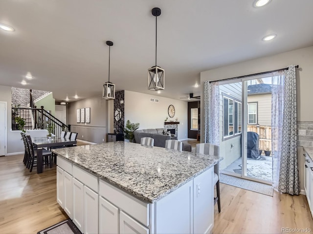 kitchen featuring pendant lighting, white cabinets, light hardwood / wood-style flooring, a fireplace, and a kitchen island