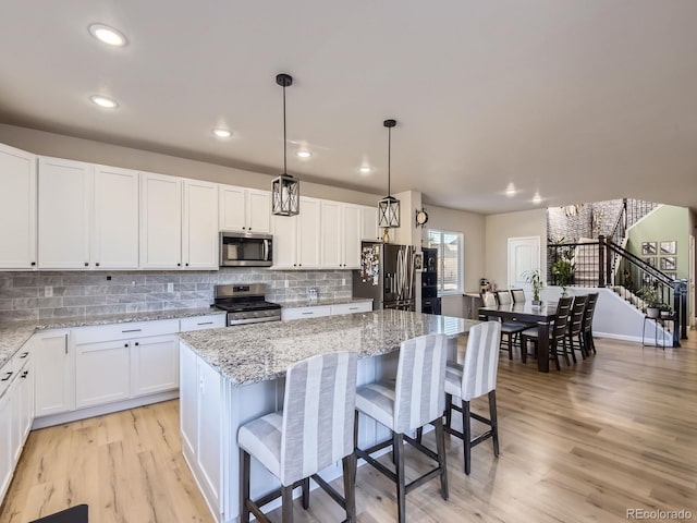 kitchen featuring white cabinets, stainless steel appliances, a kitchen island, and light hardwood / wood-style flooring