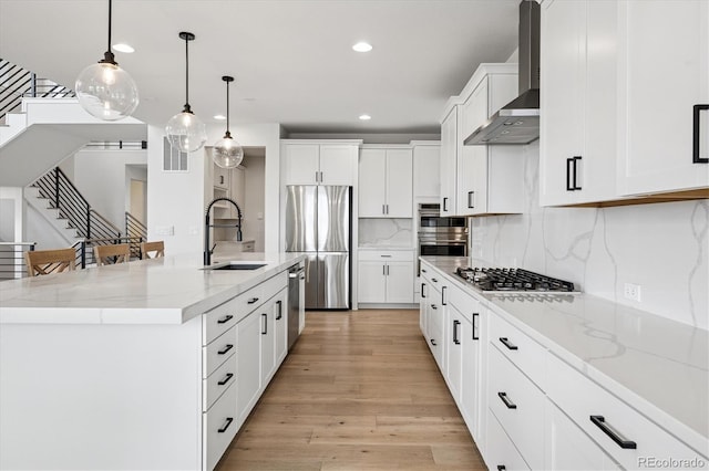kitchen featuring light wood-style flooring, a sink, wall chimney exhaust hood, stainless steel appliances, and recessed lighting
