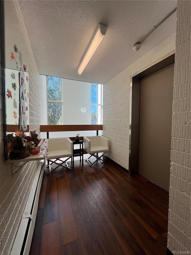 interior space featuring a textured ceiling, dark hardwood / wood-style floors, a baseboard heating unit, and brick wall