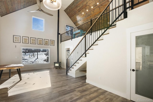 entrance foyer featuring ceiling fan, hardwood / wood-style floors, wooden ceiling, a high ceiling, and a wood stove