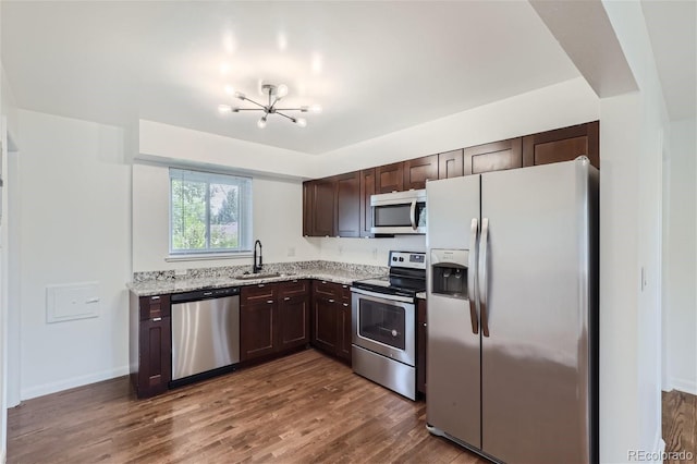 kitchen with dark hardwood / wood-style floors, stainless steel appliances, light stone counters, and sink