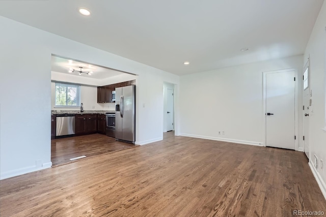 unfurnished living room with recessed lighting, a sink, baseboards, and wood finished floors