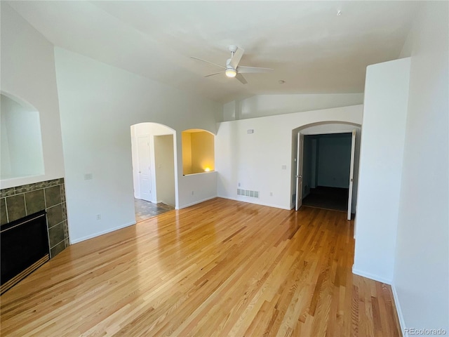 unfurnished living room with vaulted ceiling, a tile fireplace, light wood-type flooring, and ceiling fan