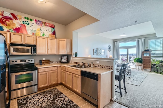 kitchen with light brown cabinets, a peninsula, appliances with stainless steel finishes, and a sink