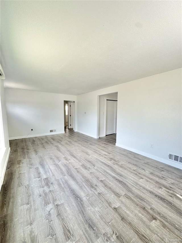 unfurnished living room featuring baseboards, wood finished floors, and a textured ceiling