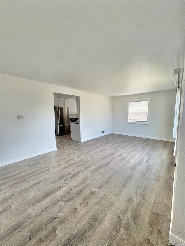 unfurnished room featuring light wood-type flooring, a textured ceiling, and baseboards
