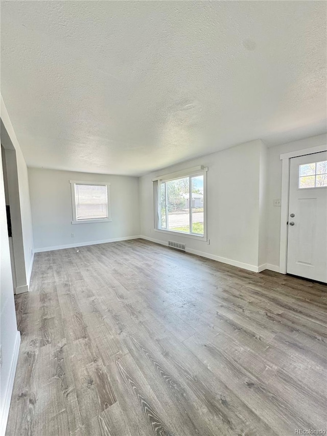 unfurnished living room featuring a textured ceiling, wood finished floors, and baseboards