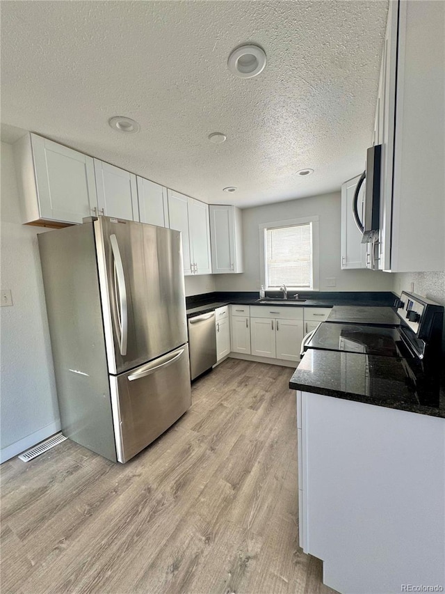 kitchen with stainless steel appliances, white cabinetry, light wood-type flooring, dark countertops, and a textured ceiling