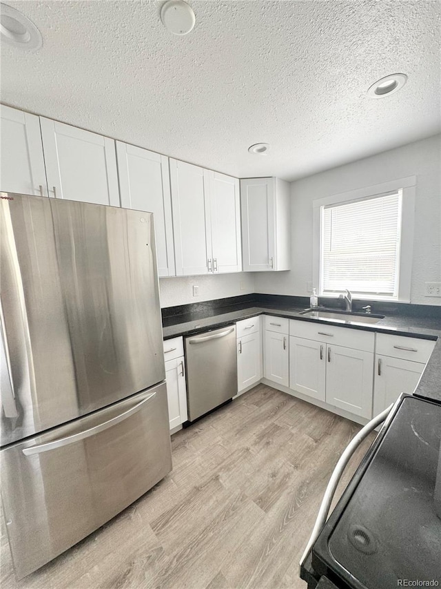kitchen featuring appliances with stainless steel finishes, a sink, a textured ceiling, white cabinetry, and light wood-style flooring