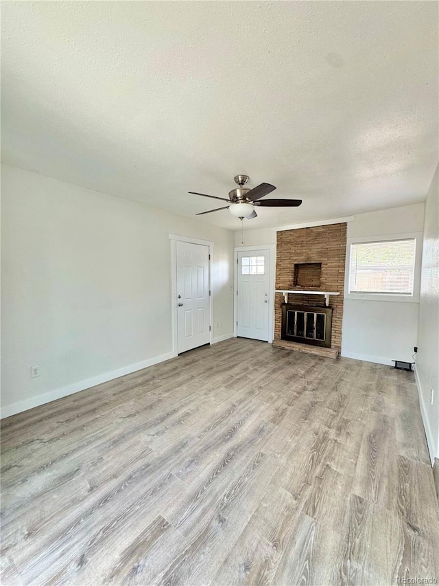 unfurnished living room featuring a textured ceiling, light wood finished floors, a ceiling fan, baseboards, and a fireplace