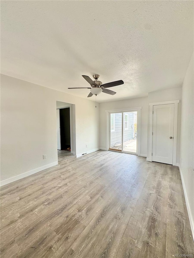 spare room with a textured ceiling, light wood-style floors, baseboards, and a ceiling fan