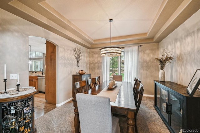 dining space featuring arched walkways, a raised ceiling, baseboards, and a chandelier