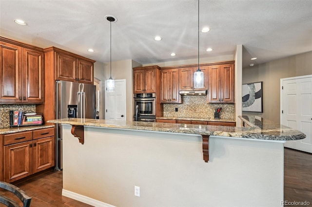 kitchen with appliances with stainless steel finishes, dark wood finished floors, a kitchen breakfast bar, tasteful backsplash, and brown cabinets