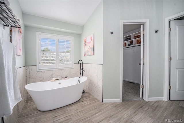 17548 E Wesley Pl, Aurora, CO 80013 - bathroom featuring a freestanding bath, tile walls, a walk in closet, wainscoting, and wood finished floors