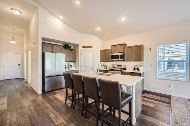 kitchen with high vaulted ceiling, sink, hanging light fixtures, stainless steel appliances, and a center island with sink