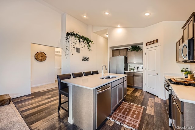 kitchen with a kitchen bar, sink, appliances with stainless steel finishes, dark hardwood / wood-style flooring, and a kitchen island with sink