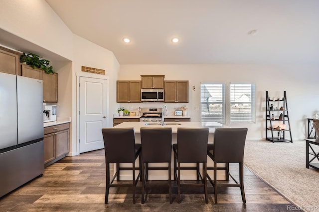 kitchen with appliances with stainless steel finishes, a breakfast bar, sink, dark colored carpet, and a center island with sink