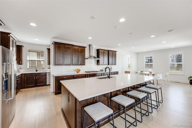 6677 Crossbridge Cir, Castle Pines, CO 80108 - kitchen with wall chimney exhaust hood, appliances with stainless steel finishes, a sink, an island with sink, and light wood-style floors