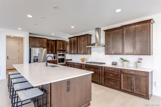 6677 Crossbridge Cir, Castle Pines, CO 80108 - kitchen featuring appliances with stainless steel finishes, wall chimney exhaust hood, a sink, a breakfast bar, and dark brown cabinetry