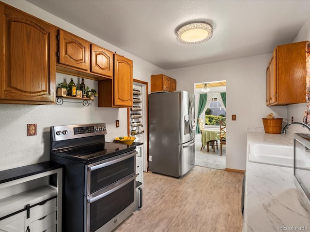6801 W 52nd Ave, Arvada, CO 80002 - kitchen featuring stainless steel appliances, light wood-style floors, brown cabinetry, a sink, and baseboards